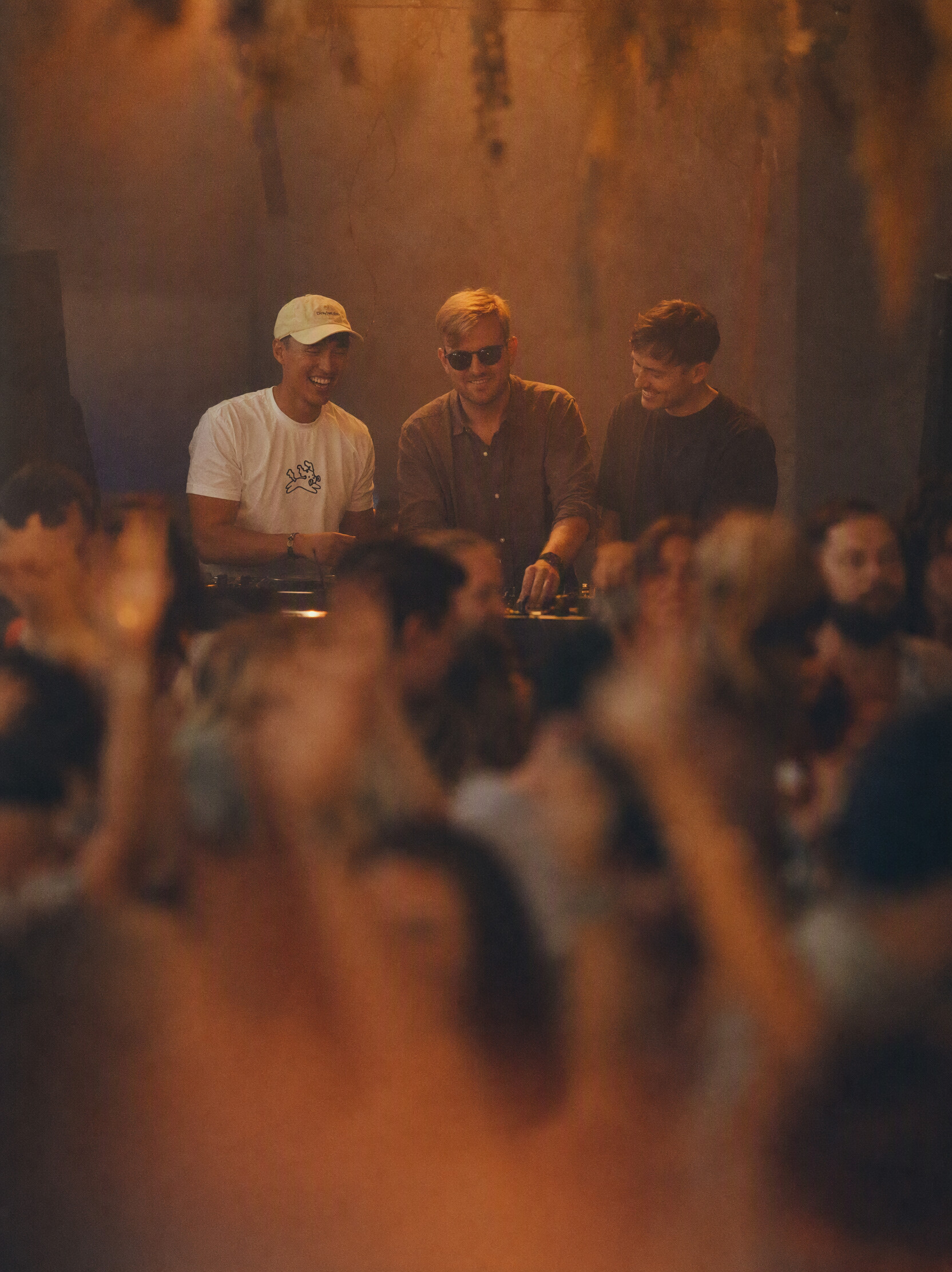 LHR — the three members behind the decks in amber light, crowd in the foreground