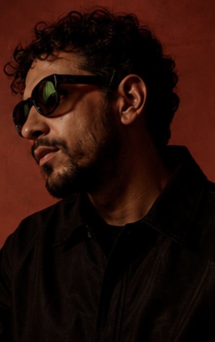 Tonnage — profile portrait in dark jacket and tinted glasses against a deep red wall